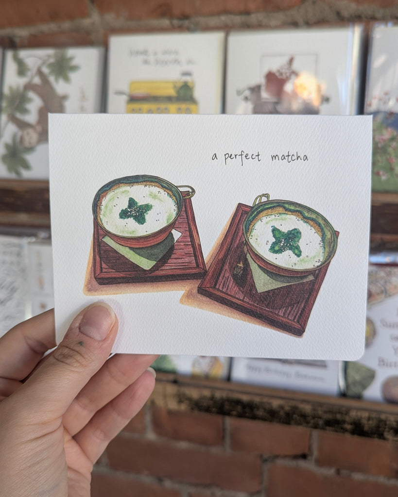 Card with illustrations of matcha cups held by a hand against a brick wall background.