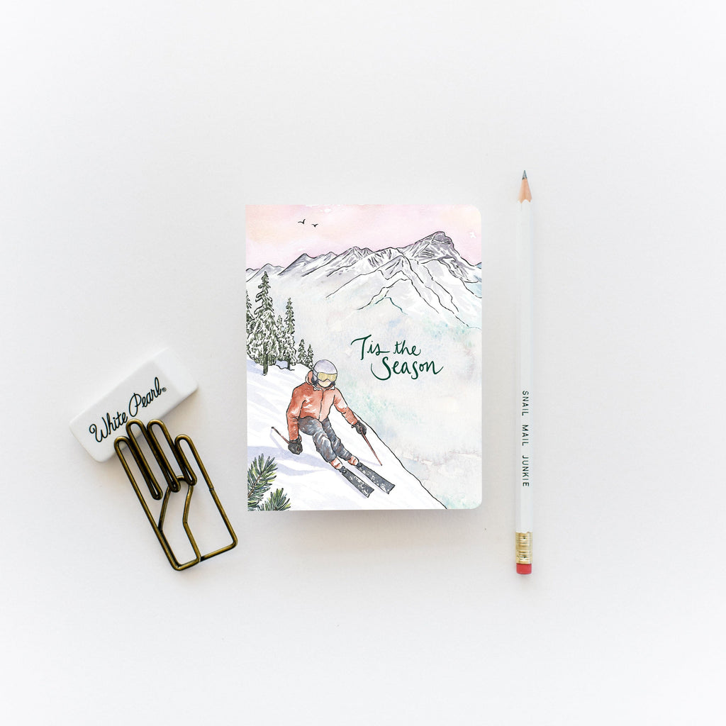 Greeting card with a winter-themed cover featuring a skier, placed on a white surface with a pen and paper clips.