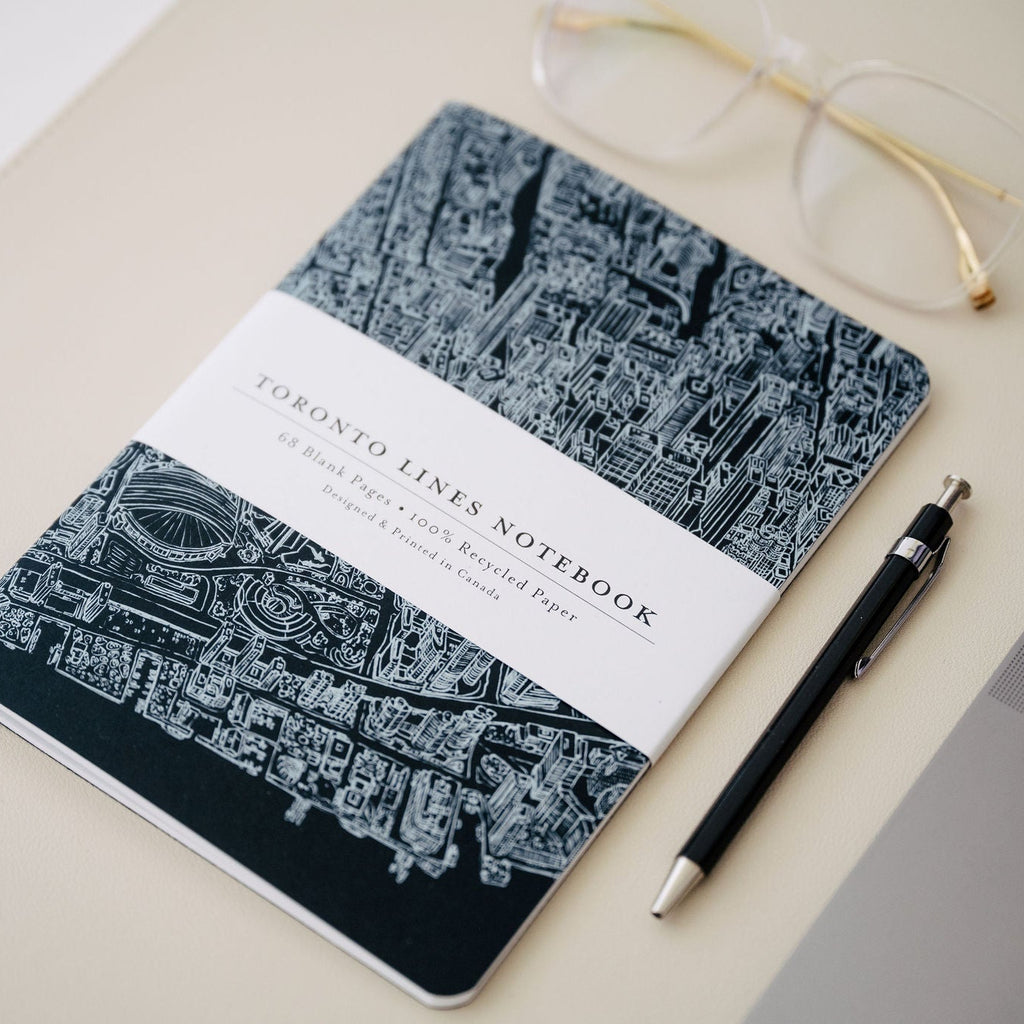 Notebook with cityscape design, pen, and glasses on a light surface