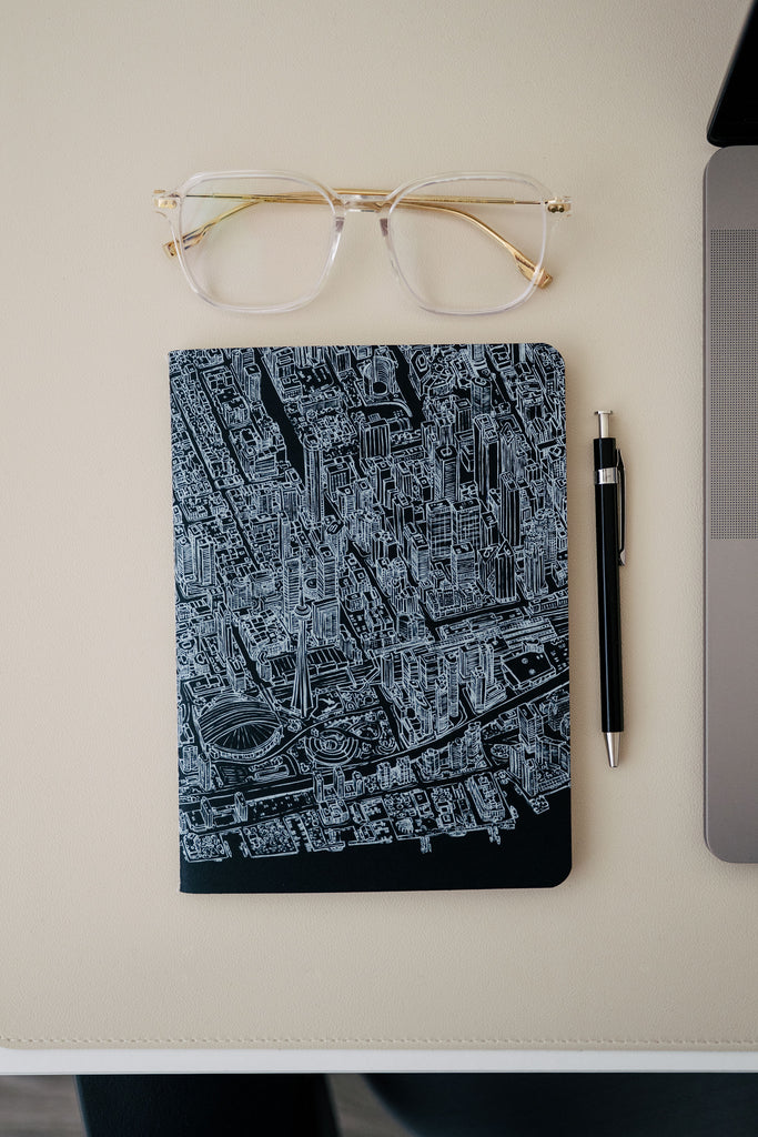 Notebook with city map design, glasses, and pen on a light surface