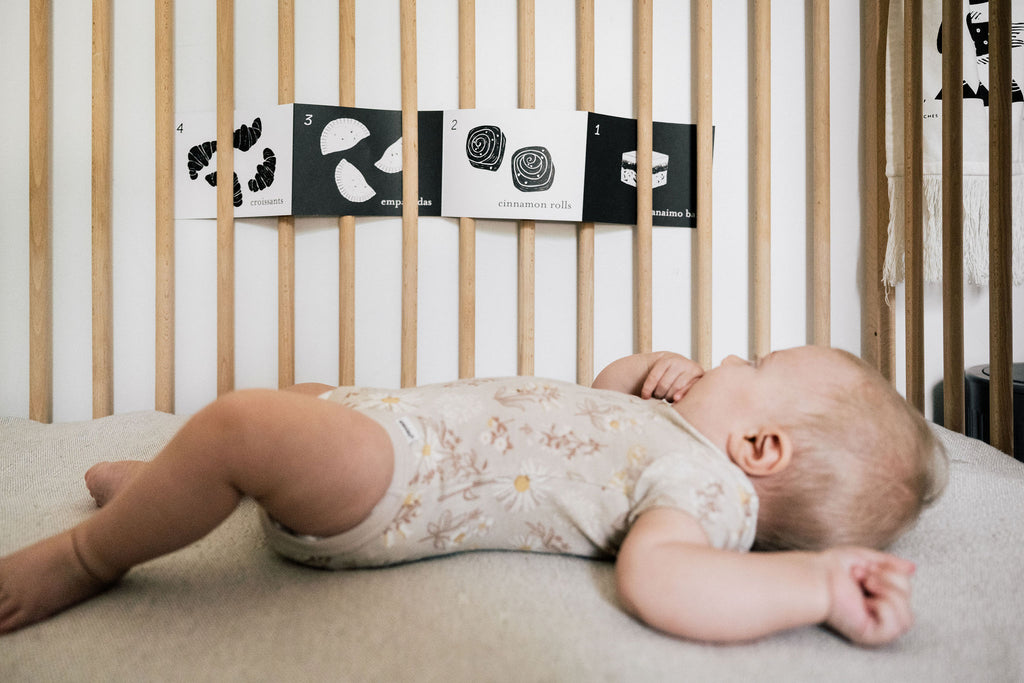 Baby lying in a crib with an accordion card presented within wooden bars.