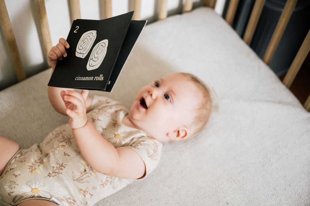Baby lying in a crib holding a card with cinnamon roll illustrations
