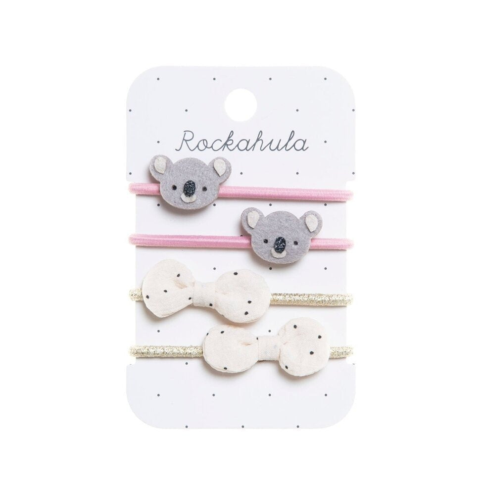 A white card with four hair ties. The first two are pink with felt koala faces. The second two are shimmery gold with white polka dot bows.