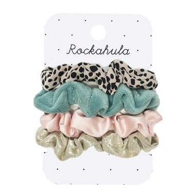 A white card displaying four hair scrunchies. One is leopard print, the second a plush turquoise fabric, the third is a sheer pink satin, and the fourth is sparkly gold.