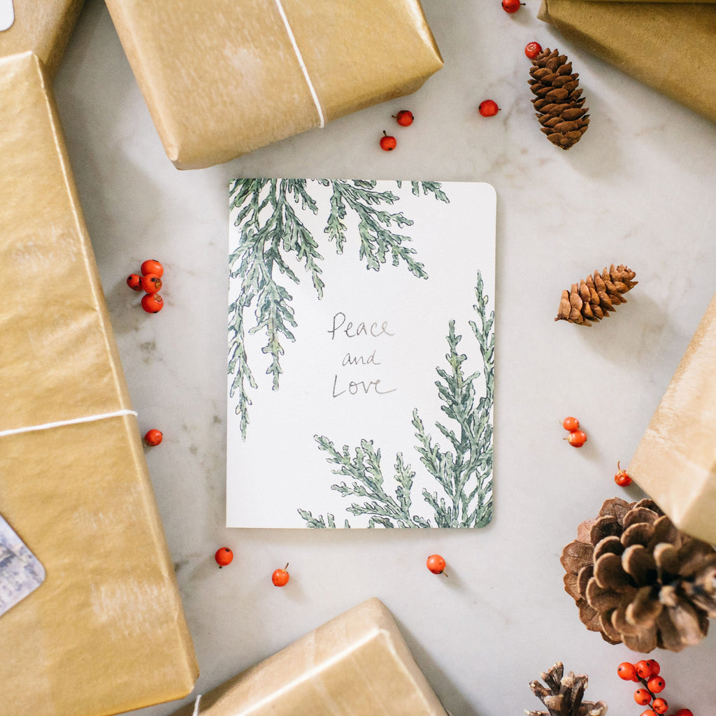 Juniper peace greeting card, surrounded by brown paper parcels and pinecones.