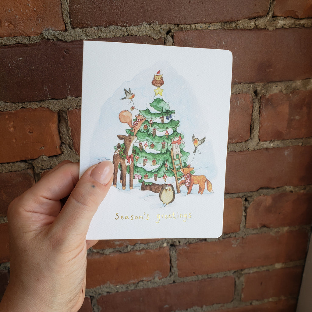 A hand holds the Forest Friends card in front of a brick wall.