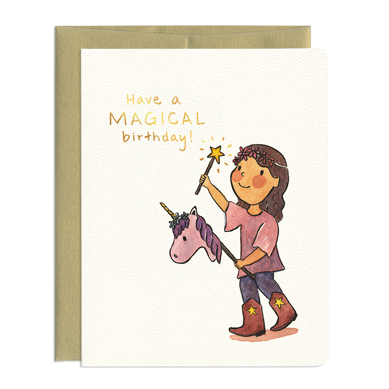 Card front features a watercolour image of a child with long hair carrying a magic wand riding a hobby-horse style unicorn. Foiled, hand-lettered text reads: Have a magical birthday!