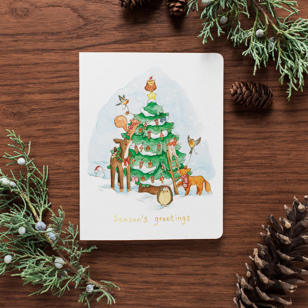 The Forest Friends card is on a wooden table surrounded by pinecones and holly.