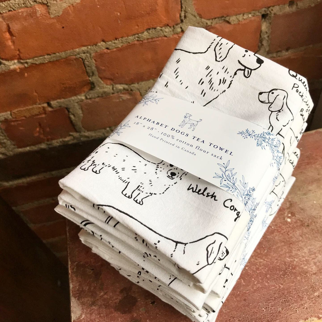 Stack of about six white cotton towels featuring drawings of dogs. Each towel is wrapped with a paper band.