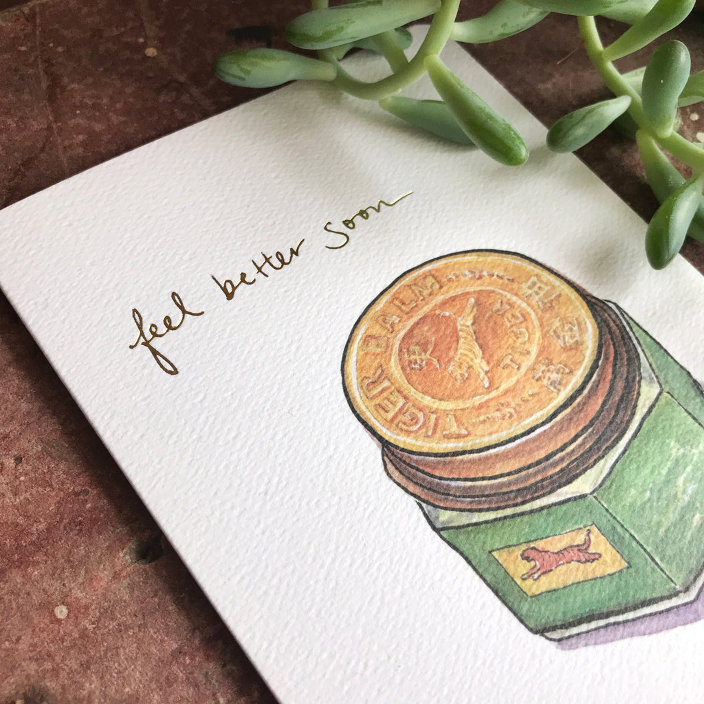 Close up of the Feel Better Tiger card resting on a wooden shelf near a jade plant.