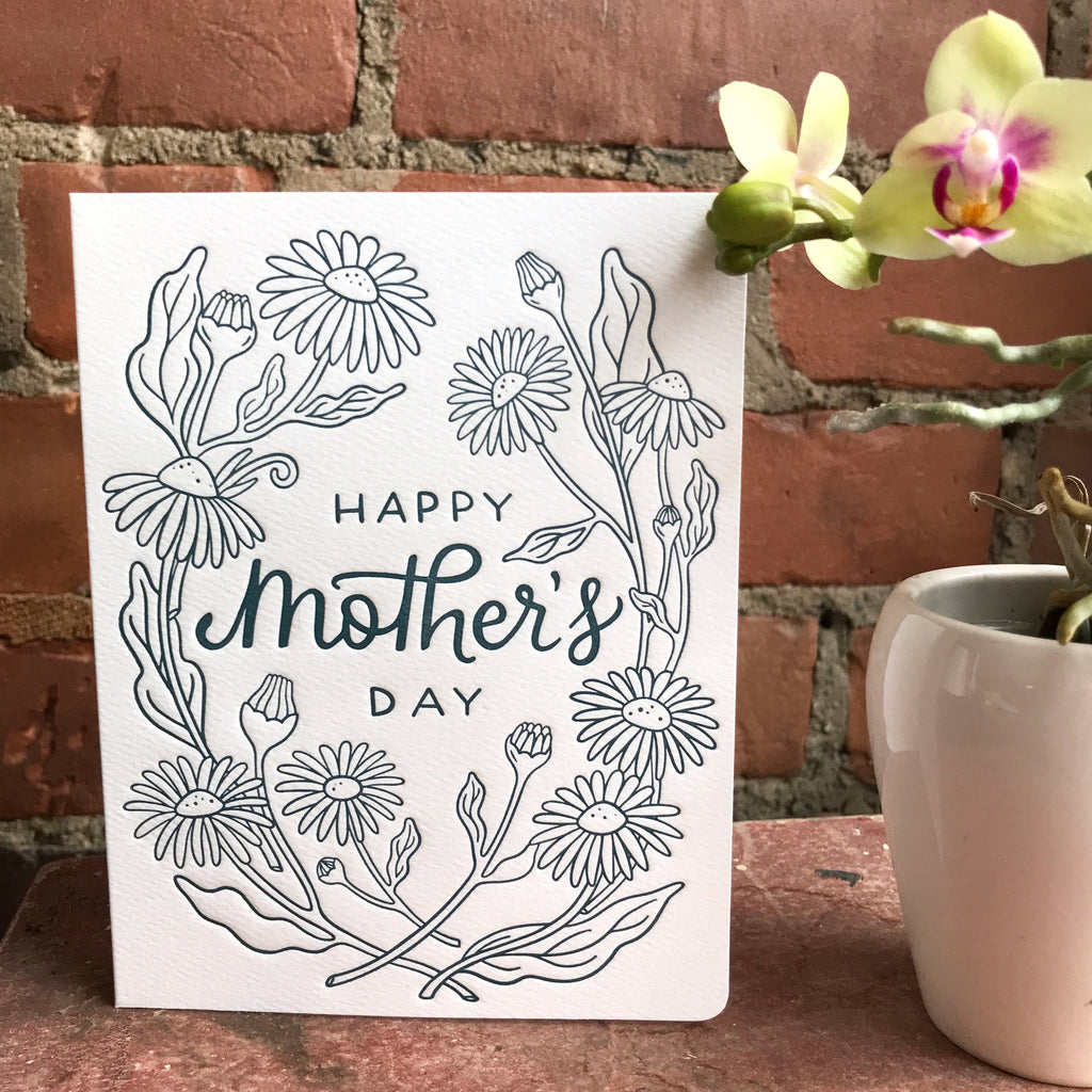 The Black-Eyed Susan Mother's Day Card sits in front of a brick wall near a plant.