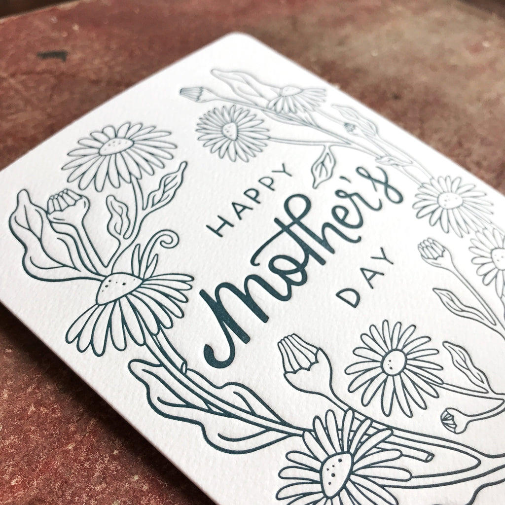 Card cover features an elegantly letter-pressed illustration of black-eyed susans in rich, dark blue on white card stock. Hand-lettered script reads: Happy Mother's Day.