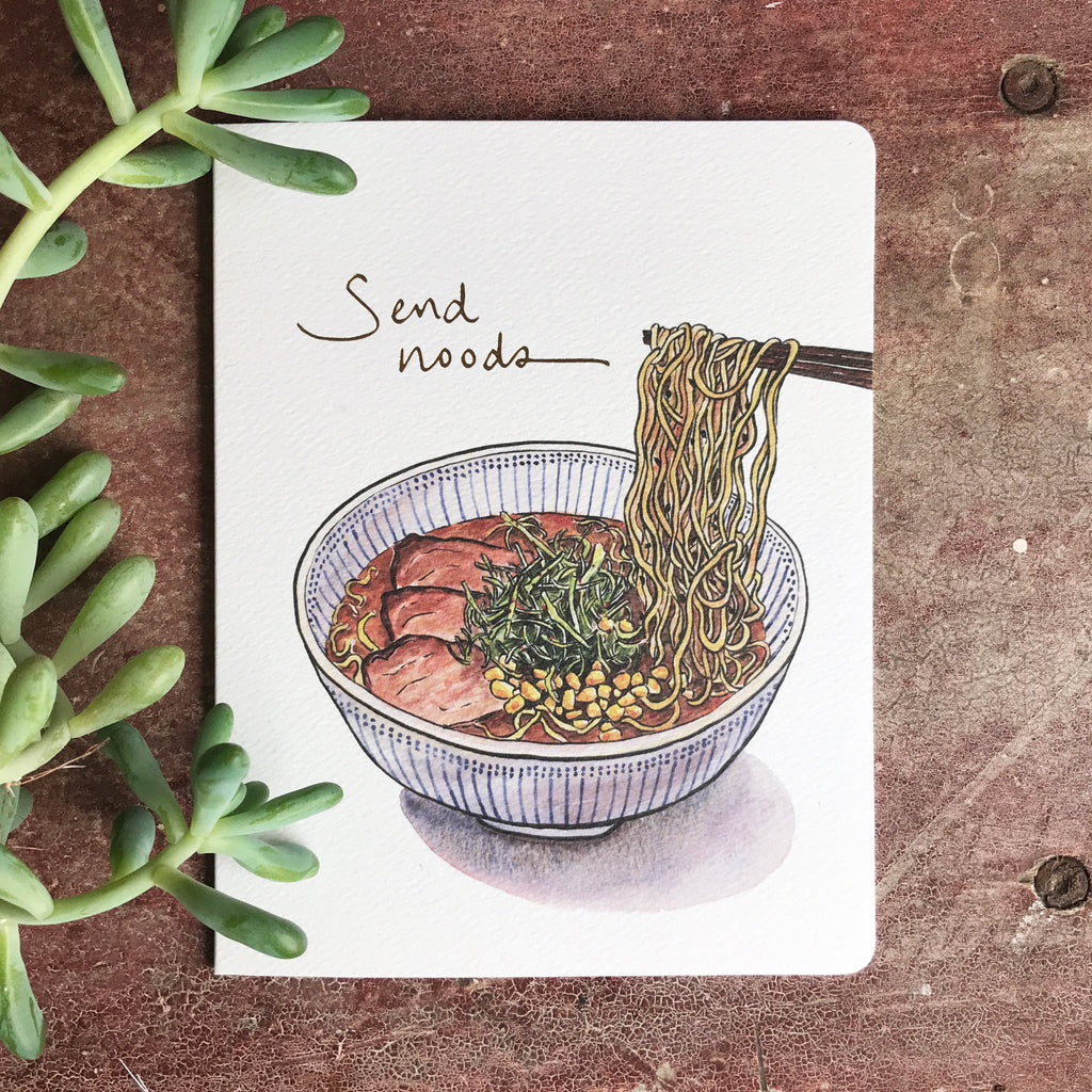 The Send Noods card rests on a wooden shelf near a jade plant.